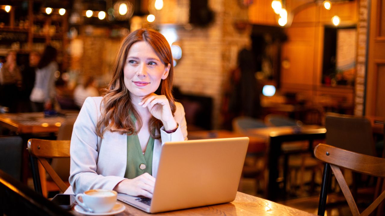 Woman working remotely in a cafe with laptop and coffee